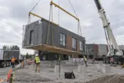 Crane and crew setting a commercial modular building section on prepared foundations
