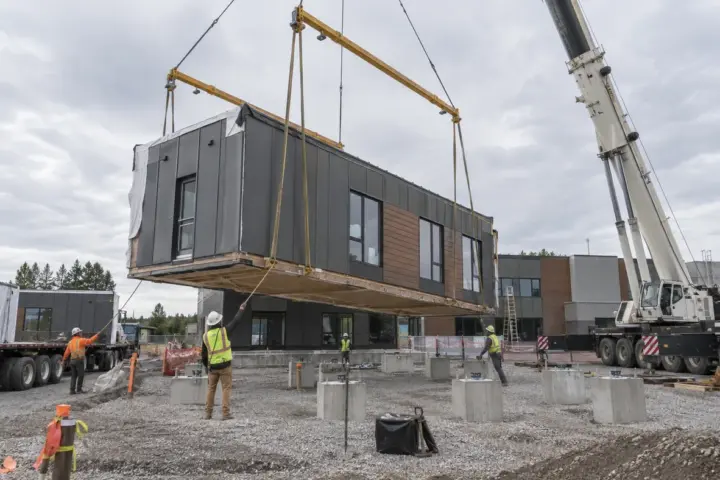 Crane and crew setting a commercial modular building section on prepared foundations