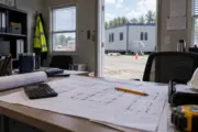 Floor plan paperwork and a calculator with a modular building visible beyond the doorway